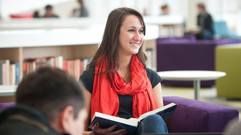 An NC State undergraduate wearing a red scarf looks up from her book at the Hunt Library.